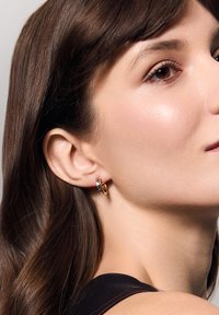 Złote i srebrne kolczyki w kształcie obręczy prezentowane na uchu modelki. Kolczyk charakteryzuje się błyszczącą, gładką powierzchnią oraz minimalistycznym wzornictwem.