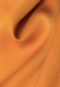 Tejido naranja texturizado con un acabado suave, mostrando sutiles reflejos y pliegues caídos, transmitiendo una calidad ligera y suave.