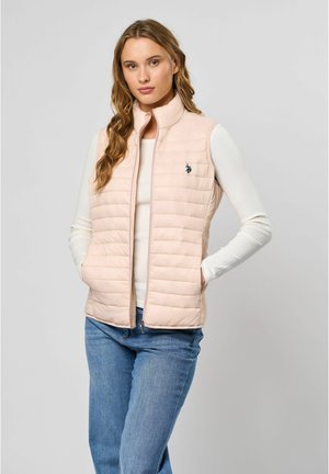 Helle rosa gepolsterte Weste mit vertikalem Steppdesign, hohem Kragen und dunkelblauem Logo. Getragen über einem weißen, gerippten Langarmoberteil und blauen Jeans.