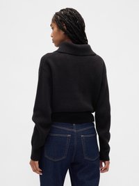 Pull en tricot noir avec un large col et un ourlet côtelé, associé à un jean en denim foncé. Le pull présente des manches longues et un tissu texturé.
