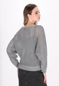 Maglione aperto grigio chiaro, dal taglio ampio e con maniche larghe. L'orlo e il colletto a coste aggiungono texture; il motivo a maglia trasparente mette in risalto il design.