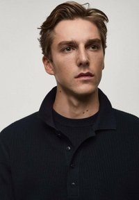 Black ribbed knit polo shirt with three buttons, short collar, worn over a matching black crewneck. Smooth texture, fitted design.