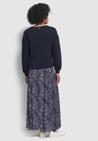 Felpa navy con spalle abbassate, abbinata a una lunga gonna a fantasia in blu scuro e bianco paisley. Sneakers bianche con dettagli dorati.