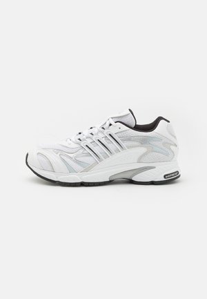 Scarpa sportiva bianca realizzata in mesh e materiali sintetici. Presenta una punta arrotondata, accenti neri e una suola intermedia grigia visibile con il marchio "adiPRENE".