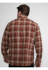 Rode en bruine geruite flanellen shirt met lange mouwen, knoopmanchetten en een rugpanddetail. Zachte textuur en het geruite patroon is zichtbaar.