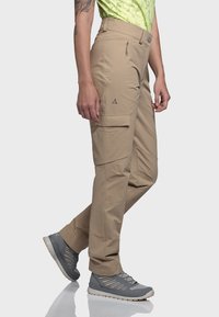 Beige Cargo-Hosen mit Reißverschlusstaschen und schlankem Design, kombiniert mit grauen Sportschuhen mit strukturiertem Obermaterial und leichtem Sohlen.
