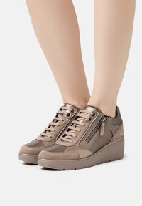Zapatillas beige con materiales mixtos, incluyendo ante y cuero liso, con cierre de cordones y cremallera lateral en una suela de cuña.