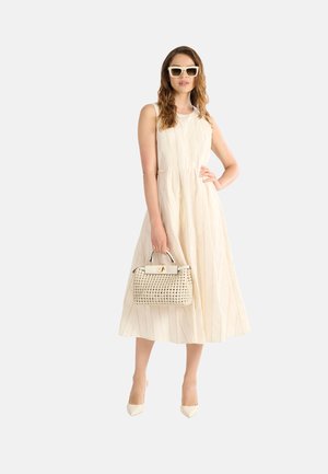 Abito beige chiaro senza maniche con righe verticali, lunghezza al ginocchio. La modella tiene una borsa intrecciata e indossa occhiali da sole bianchi a forma quadrata con tacchi a spillo.