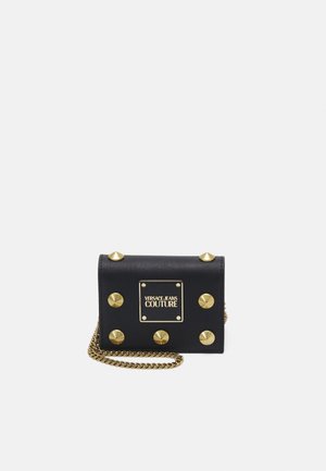 Czarny portfel Versace Jeans Couture z złotymi ćwiekami, tabliczką z logo i złotym łańcuszkiem na białym tle.