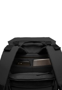 Sac à dos noir avec une ouverture en haut, dotée de bretelles rembourrées et de plusieurs compartiments. L'intérieur comprend des poches en mesh et une section zippée.