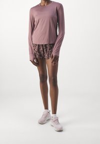 Langærmet mauve top, mønstrede brune shorts og lyserøde sneakers. Har løs pasform og bløde stoftekster.