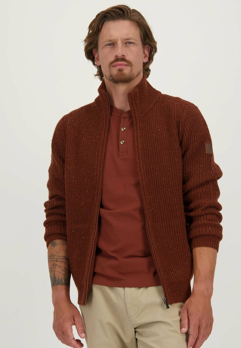 Bruine gebreide zip-up trui met een hoge kraag, geribbelde textuur en lange mouwen, gedragen over een bordeauxrood shirt en gecombineerd met lichtbeige broek.