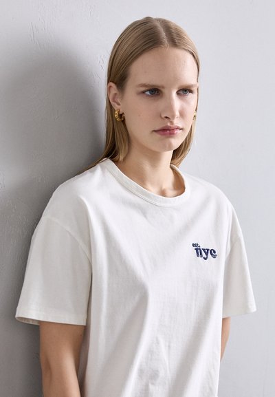 White cotton t-shirt with short sleeves, featuring navy blue embroidered text "est. nyc" on the left chest. Soft, casual fit.