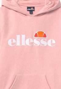 Haut de survêtement rose clair avec un grand logo "ellesse" blanc et un demi-cercle orange et blanc au-dessus. Comprend une poche avant et un cordon de serrage.