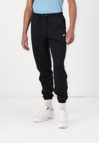 Černé bavlněné tepláky s elastickým pasem, staženými kotníky a malým bílým logem Nike na levé stehně. Nosit s bílými teniskami.