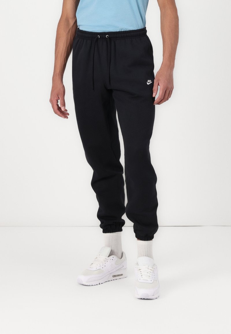 Černé bavlněné tepláky s elastickým pasem, staženými kotníky a malým bílým logem Nike na levé stehně. Nosit s bílými teniskami.