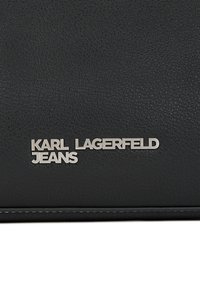 Melnas ādas maciņš ar teksturētu virsmu, sudraba logotipa detaļa ar uzrakstu "KARL LAGERFELD JEANS" un baltas šuves akcentiem.