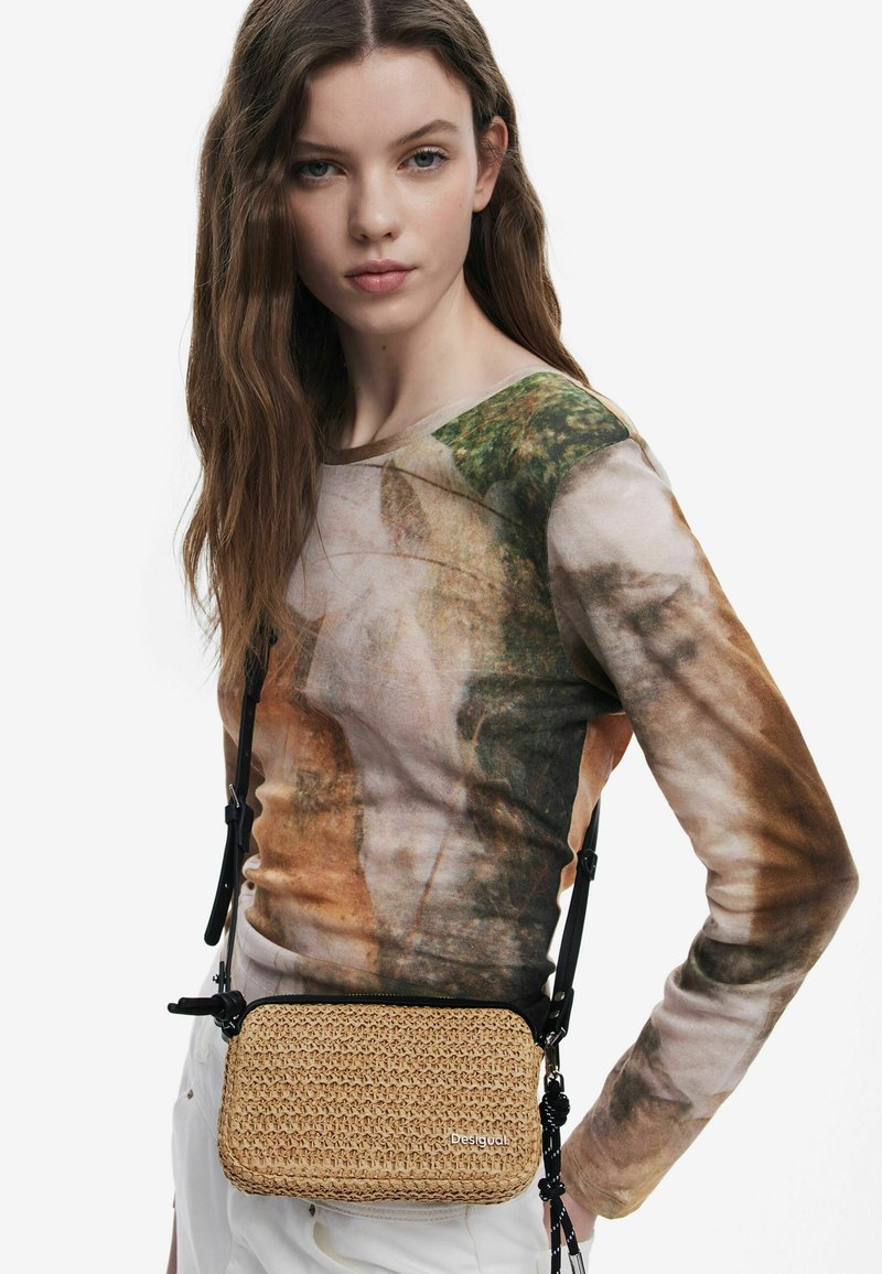 Borsa a tracolla in paglia intrecciata con forma rettangolare e chiusura a zip, dotata di cinturini regolabili neri e un dettaglio logo discreto.