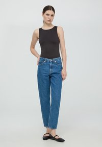 Czarny bezrękawnik połączony z niebieskimi, wysokiej talii spodniami o prostych nogawkach. Dżinsy mają klasyczny pięciopocketowy krój i wyblakłą teksturę.