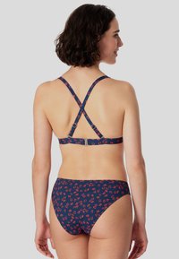 Marineblå bikini med rødt blomsterprint, udstyret med krydskorsjusterbare stropper og en spænde lukning bagpå. Glat, strækbart stof.