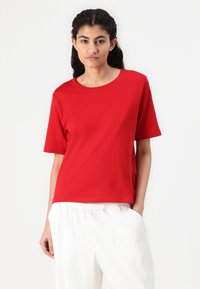 Röd t-shirt med korta ärmar i mjuk bomull, med rund halsringning och avslappnad passform, i kombination med ljusa, lösa byxor.