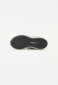 Suola di scarpa in gomma nera con motivo a nido d'ape; intersuola beige e marchio. Fondo piatto per stabilità e aderenza.