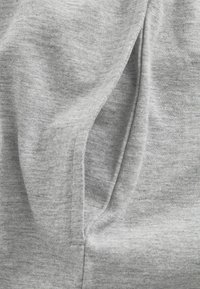 Grått tyg med en slät, något texturerad yta. Har en sida söm och veck, vilket indikerar en avslappnad, draperad design.