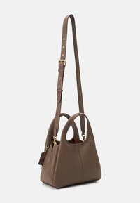 Barna bőr kézitáska rövid fogantyúkkal, állítható hosszú vállpánttal arany csatokkal és egy kis függő címkével.