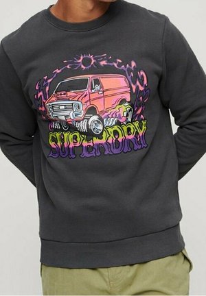 Sudadera gris oscuro con gráfico colorido de una furgoneta monstruo rosa que emite llamas y la palabra "SUPERDRY" en texto estilizado debajo.