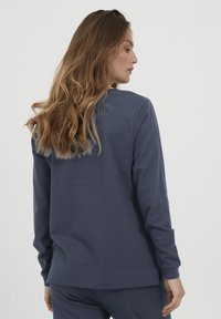 Maglietta a maniche lunghe blu navy realizzata in tessuto morbido. Presenta un colletto rotondo e spacco laterale all'orlo per un maggiore comfort e libertà di movimento.