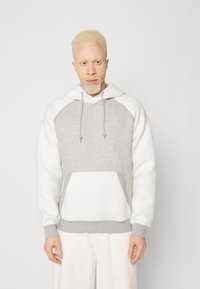 Sudadera gris y blanca con un bolsillo frontal, cordones en la capucha y puños acanalados. Tejido suave y texturizado con mangas raglán.