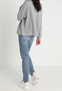 Ljusgrå sweatshirt med lös passform och rundad fåll, kombinerad med ljusblåa baggy jeans och vita sneakers. Bakifrån, avslappnade material.
