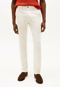 Hvide chinos med en tætsiddende pasform, der har en glat tekstur og en enkelt knaplukning. Kombinationen med brune ruskinds loafers.