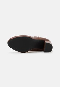 Scarpa in pelle marrone con tacco spesso, caratterizzata da una superficie liscia e una suola in gomma nera. Il design include minimi dettagli di cucitura.