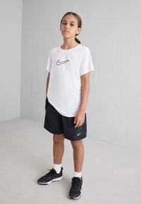 Λευκό κοντομάνικο μπλουζάκι Nike με μαύρο λογότυπο, συνδυασμένο με μαύρη βερμούδα και μαύρα αθλητικά παπούτσια. Απλή και λειτουργική αθλητική ένδυση.