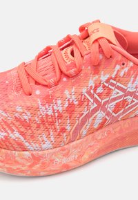 Korallenfarbenes Lauf- schuhmodell mit strukturiertem Obermaterial in Weiß und Orange, verstärkten Schnürlöchern und einer gepolsterten FF Blast+ Sohle.