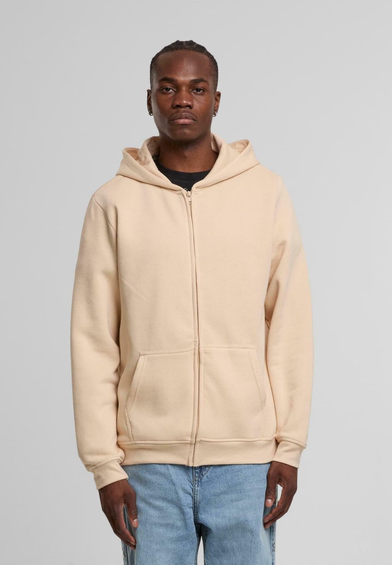 Beige zip-up hættetrøje lavet af blødt stof, med snor i hætten, lange ærmer og frontlommer. Glat tekstur, afslappet pasform.