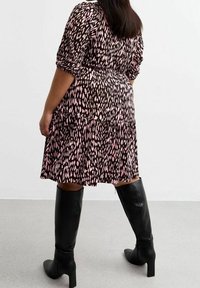 Schwarz und pink gemustertes, plissiertes Kleid mit Dreiviertelärmeln, kombiniert mit kniehohen schwarzen Stiefeln. Glatter Stoff und lässige Passform.