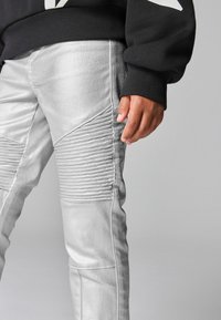 Silver denimbyxor har ribbade textursektioner på låren, skräddarsydd passform och matchas med en svart, lös passform tröja.