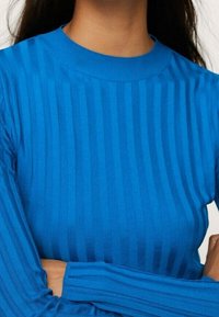 Blauer gerippter Strickpullover mit Rundhalsausschnitt und langen Ärmeln, der abwechselnde vertikale Streifen für zusätzliche Textur aufweist.