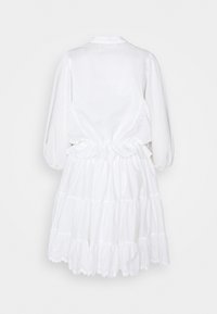 Abito bianco in cotone con vita arricciata, maniche a sbuffo, gonna a strati con balze e dettagli in pizzo all'orlo. Vista dal retro.