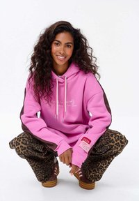 Růžová mikina s bílým nápisem a stříbrnými tkaničkami, spárovaná s kalhotami s hnědočerným leopardím potiskem. Hnědé akcenty na mikině.