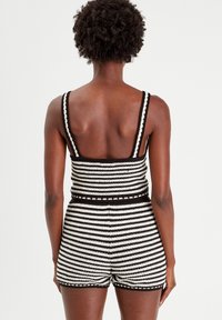 Zwart-wit gestreepte romper met brede schouderbanden, textuurstof, aansluitende taille en shorts ontwerp. Heeft geschulpte afwerkingen aan de randen.