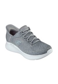 Scarpa sportiva grigia con tomaia in mesh testurizzato, lacci e suola in schiuma bianca. Presenta un logo sottile sul lato e un tallone rinforzato.
