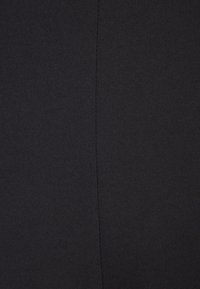 Gros plan d'un tissu noir montrant une couture verticale au centre avec une surface légèrement texturée et tissée.