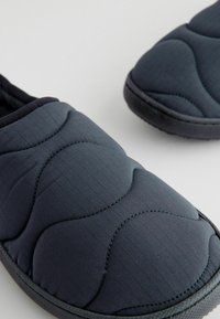 Pantofole trapuntate marine con un motivo testurizzato e suole in gomma. Caratterizzate da una parte superiore imbottita e un design slip-on per una facile vestibilità.