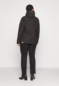 Czarna kurtka z kapturem z purpurowym wzorem w kropki, wykonana z teksturowanej tkaniny, z brązowym logo po boku. Noszona z ciemnymi dżinsami i botkami na obcasie.