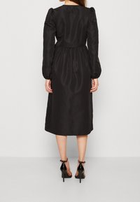 Svart satinklänning med puffade ärmar, rynkad midja och midi-längd. Bärs med svarta högklackade sandaler. Slät textur och enkel design.
