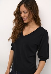 Pull en tricot noir avec un décolleté en V, des manches bouffantes et un ourlet côtelé. Le tissu semble doux avec une texture lisse.