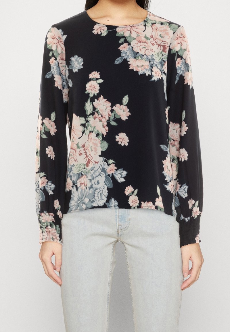 Blusa a maniche lunghe floreale in tessuto nero, con motivi di fiori rosa chiaro e blu, scollatura rotonda e polsini arricciati.